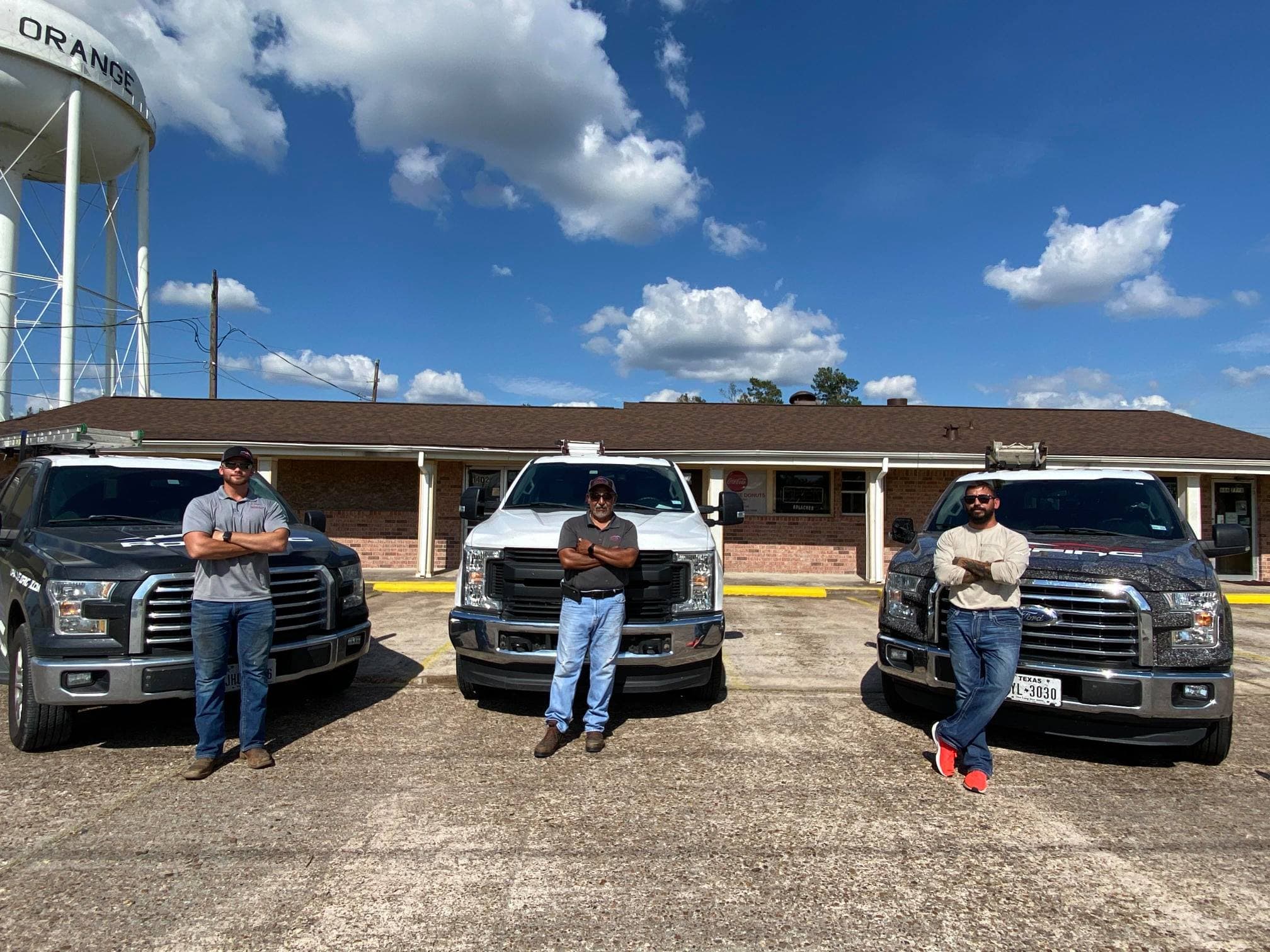 Three men standing confidently by their trucks in front of a building under a blue sky.